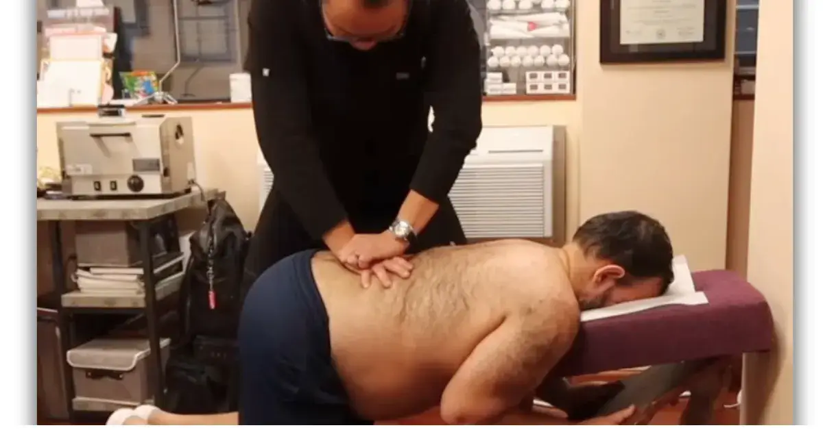 Chiropractor performing a spinal adjustment on a male patient lying face down on a treatment table.